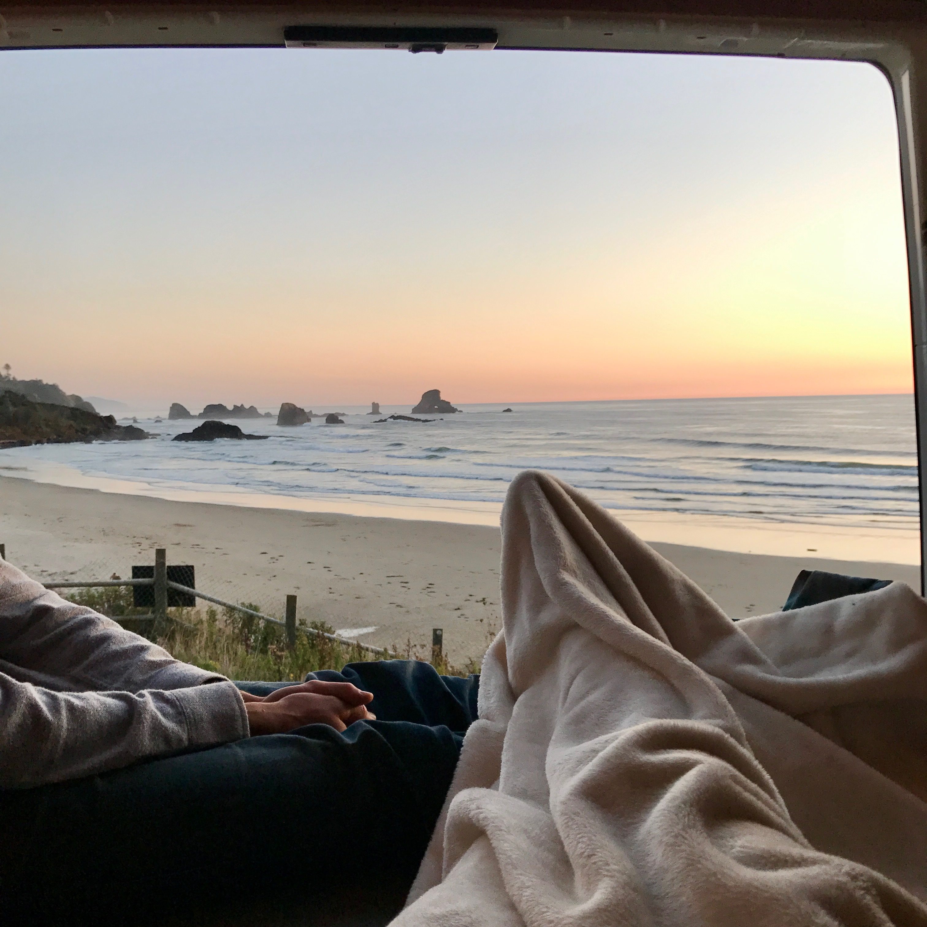 Two people looking out of van parked at beach sunset